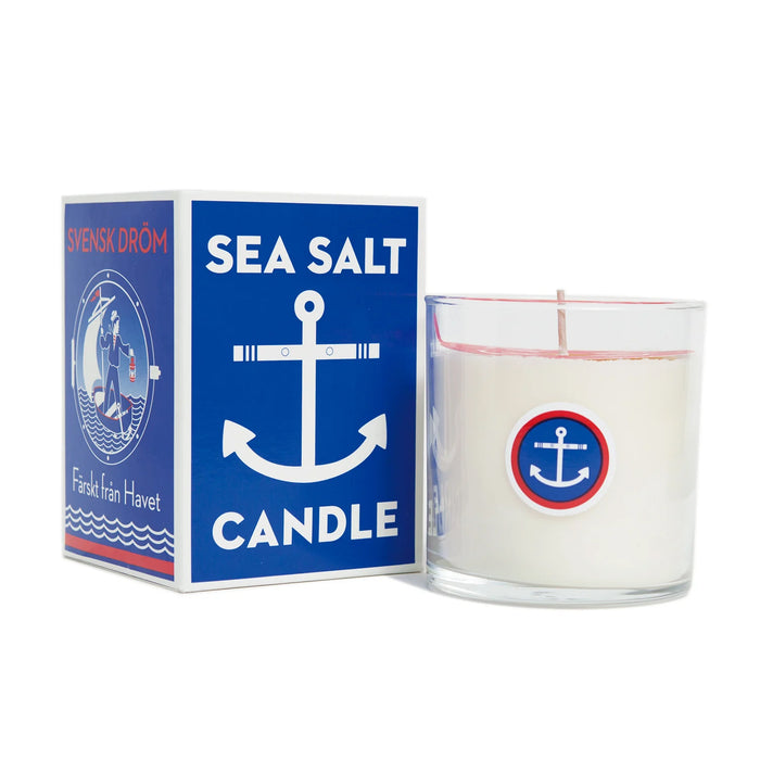 A white candle in a glass container with image of an anchor, next to a box labeled 'Sea Salt Candle'.