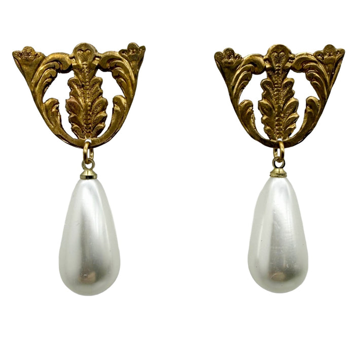 Pair of earrings with gold leaf design and white teardrop pearls on a white background