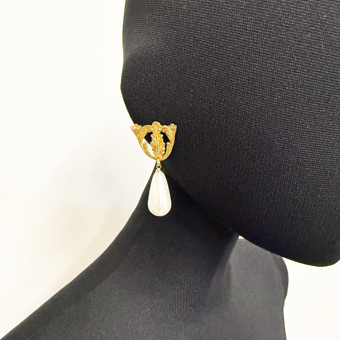 Gold earring with a teardrop-shaped pearl on a black mannequin head.