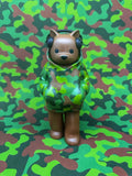 Low Fidelity - One With Nature by Luke Chueh: A 7-inch vinyl figurine of a camouflaged animal in a hoodie with headphones, blending into its patterned surroundings.