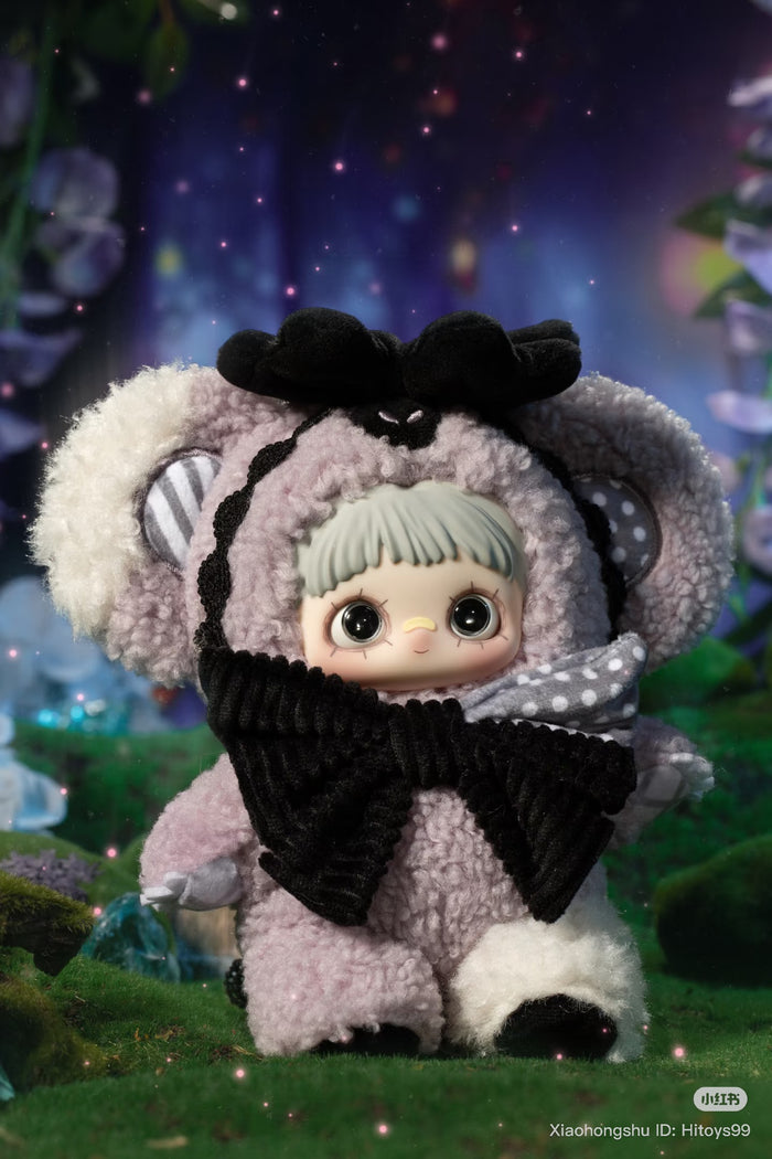 MayMei Symbiote Neverland Series doll in koala-style onesie with glittery eyes, standing on mossy-green surface, against a twinkling forest backdrop.