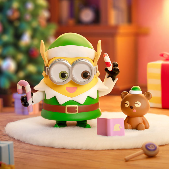 Minions Bedtime Stories figure in elf attire, holding candy canes, with teddy bear and gift box; part of a collectible series from Strangecat Toys.