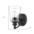 One-Light Matte Black Wall Sconce with clear tapered glass shade and curved arm design shown with dimensions of eight point two five inches high by five inches wide by six point seven five inches deep
