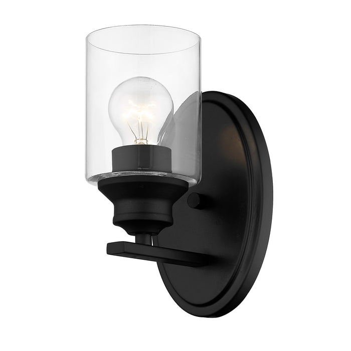 Bottom up angled view of the lighted One-light matte black wall sconce with cylindrical clear glass shade and modern backplate