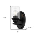 One-light matte black wall sconce with cylindrical clear glass shade and modern backplate shown with dimensions of nine point two five inches high by five inches wide by five point seven five inches deep