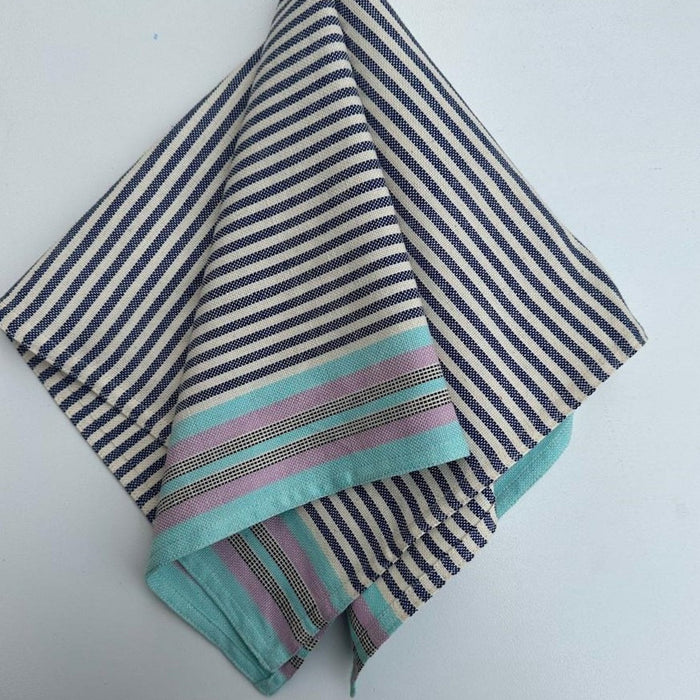 A striped cotton napkin in shades of blue, gray, and beige, handwoven and laid out folded.