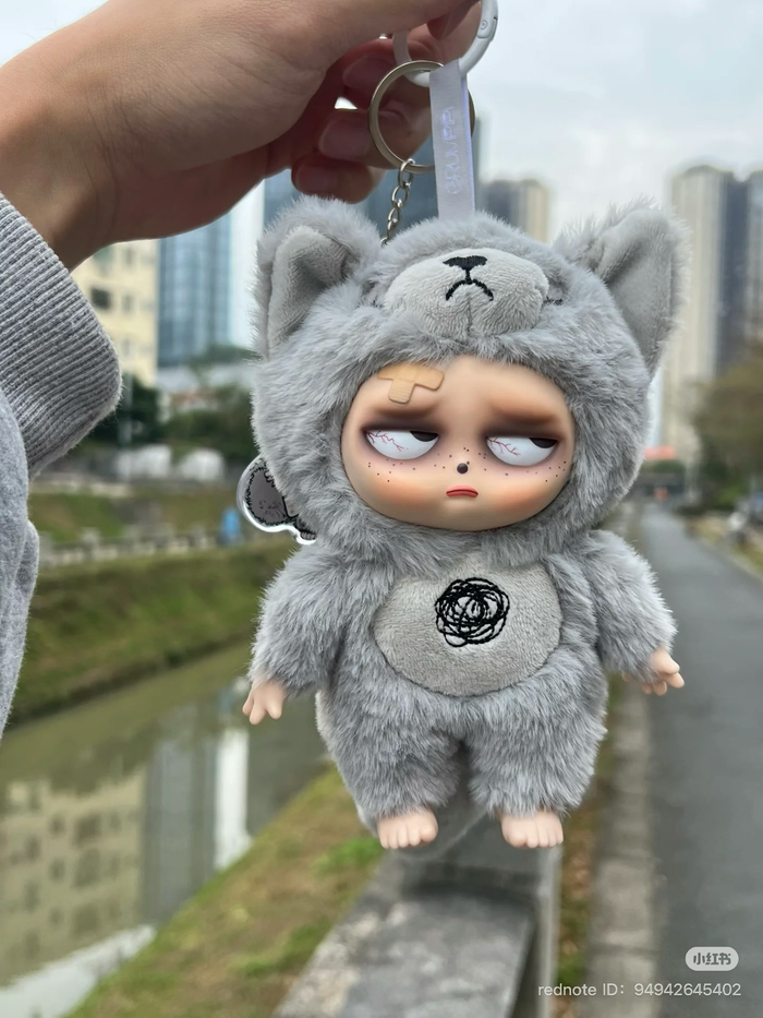 Sleepless Grumpipi Plush Blind Box Keychain, featuring a hand holding a stuffed animal, available for preorder, ships August 2025.