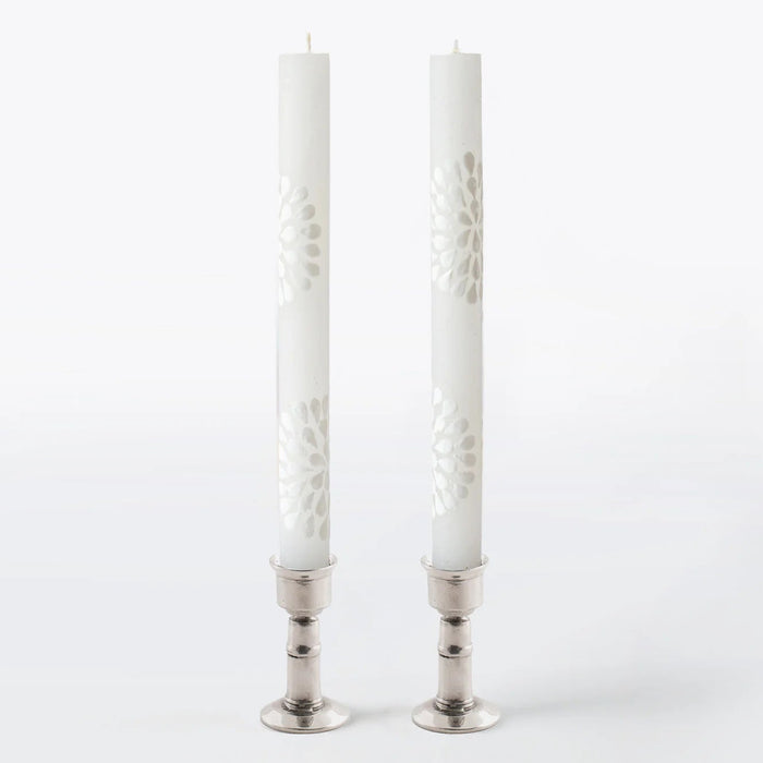 Two white candles in silver candlesticks on a white background