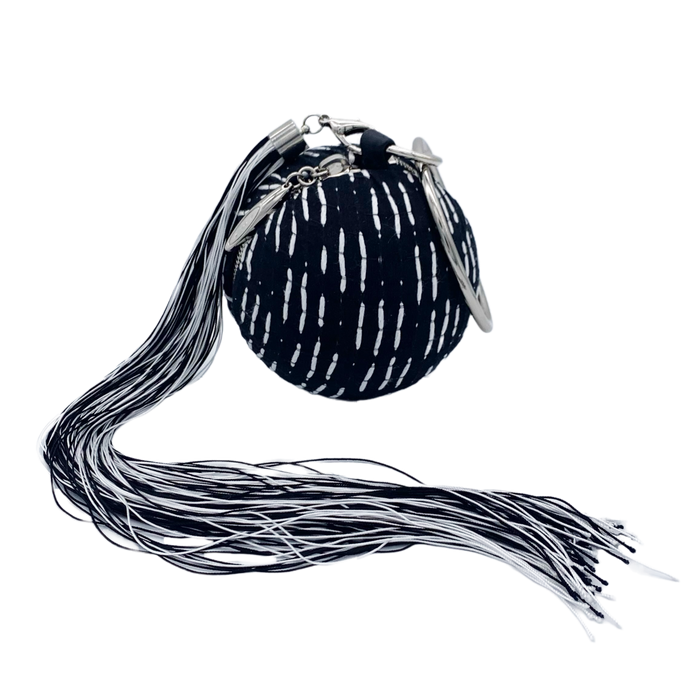 A black wristlet handbag with white stitched dashes and a removable black & white tassel, designed by Maya Luz.