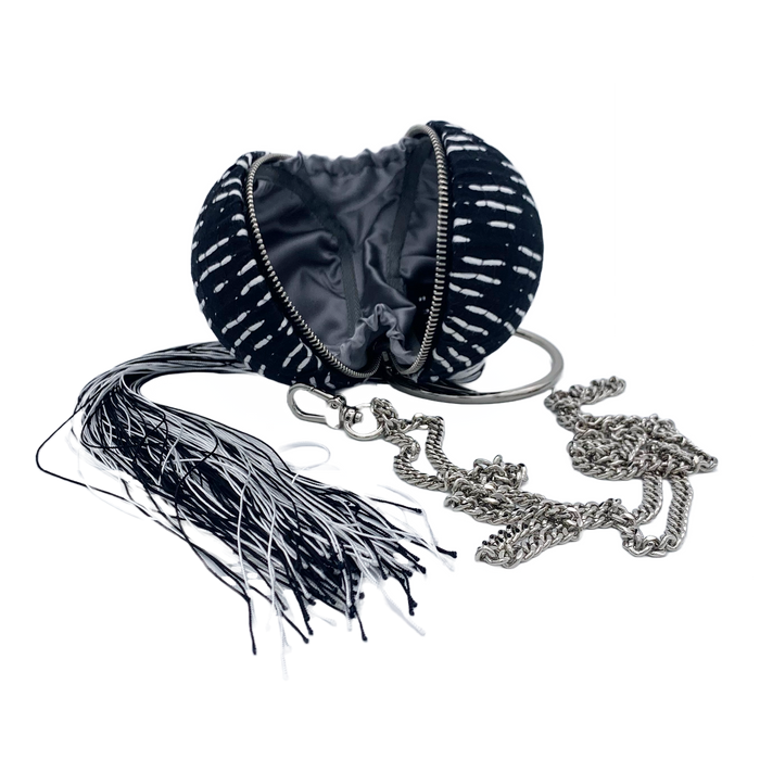 A black wristlet handbag with white stitched dashes and a removable black & white tassel, designed by Maya Luz.